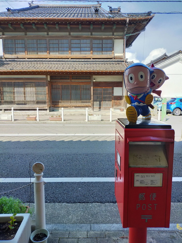 OPPO2020A_20230910090642　ハットリくんとシンちゃん。赤いポストの上、そして立派な日本建築の家屋が背景。映えますねえ。　